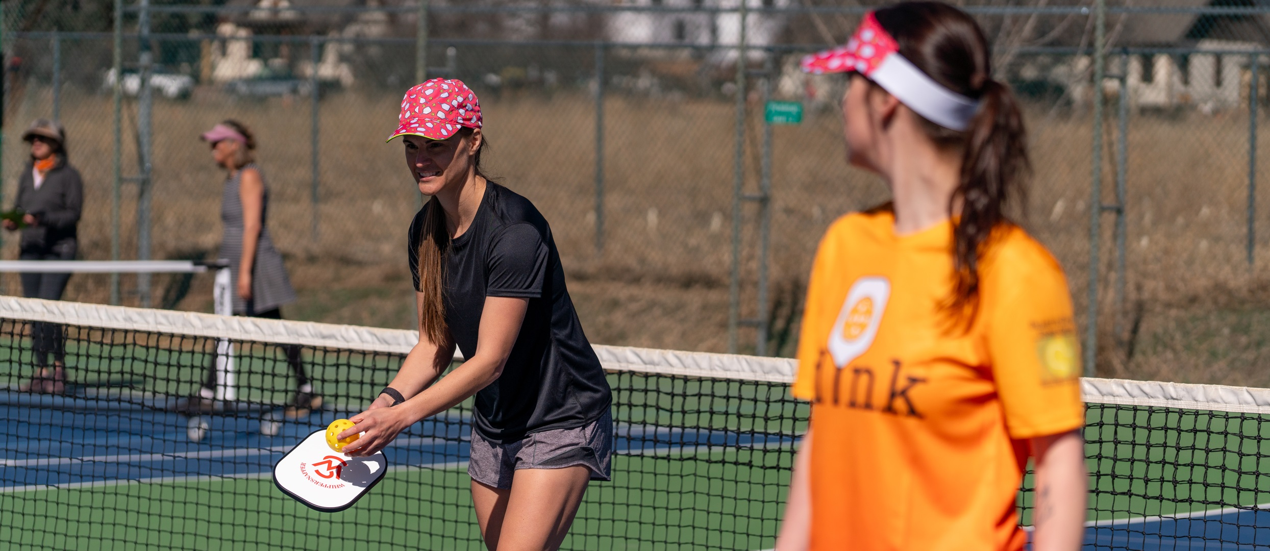 Two Players wearing a pink pickleball hat and visor during a match.