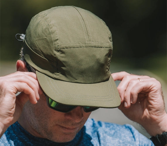 Person wearing a green elite running hat and sunglasses with a blurred background