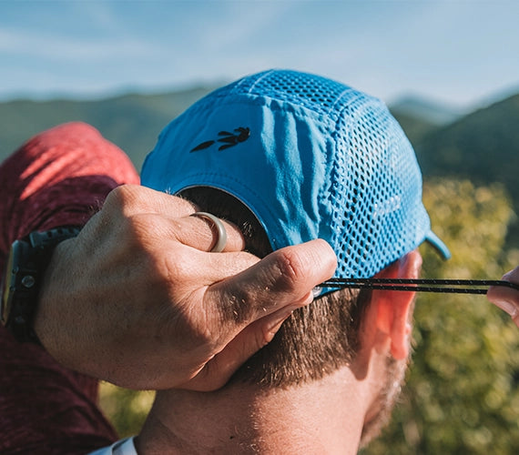 Person adjusting a blue elite crusher hat outdoors with mountains in the background